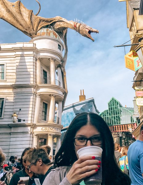 kathy drinking butter beer at Diagon Alley with Dragon behind her