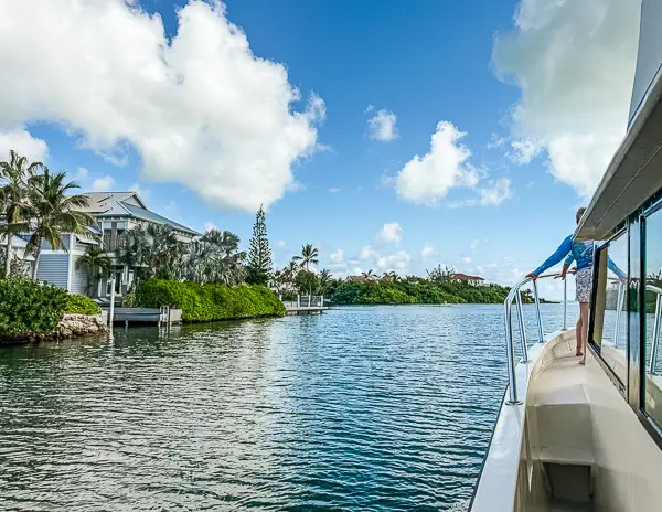 Boat cruising out of the marina in Grand Cayman, passing waterfront homes under a bright blue sky.