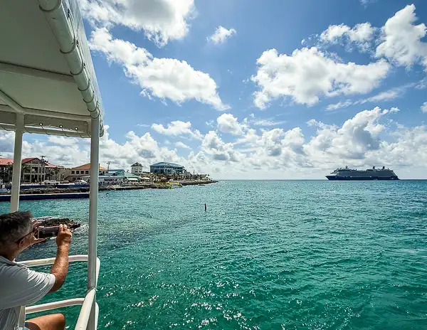 View from a tender boat approaching George Town, Grand Cayman, with a cruise ship anchored offshore under a bright blue sky.