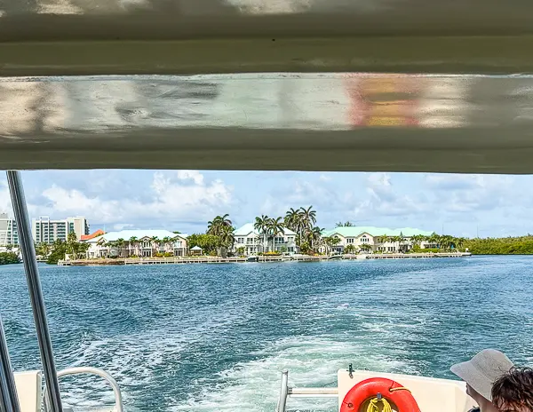 View from the back of a boat in Grand Cayman with waterfront villas along the shoreline and open water ahead.