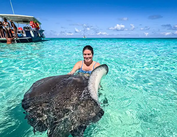 Woman (Kathy) holding a large stingray in the clear turquoise water at Stingray City sandbar in Grand Cayman on a sunny day.