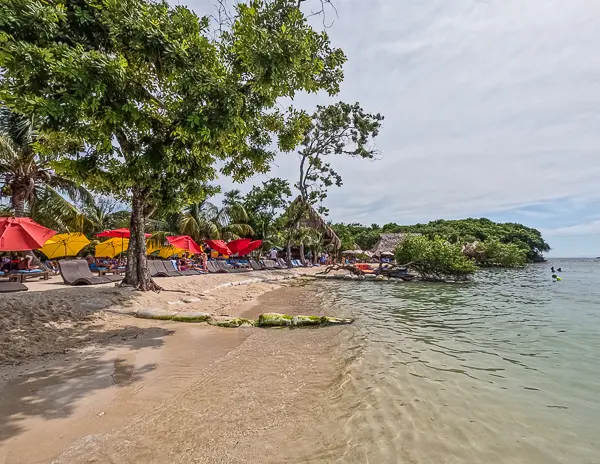 Beach at Brady’s Cay in Roatán, Honduras with colorful umbrellas, lounge chairs, and calm Caribbean water.