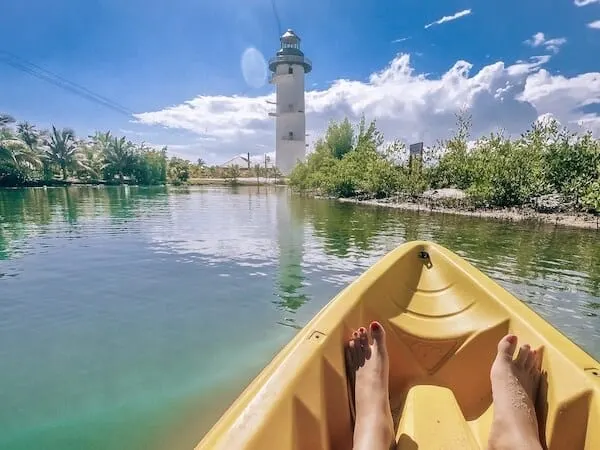 Tip of a yellow kayak and a pair of feet pointing towards the lighthouse over the lagoon at Harvest Caye