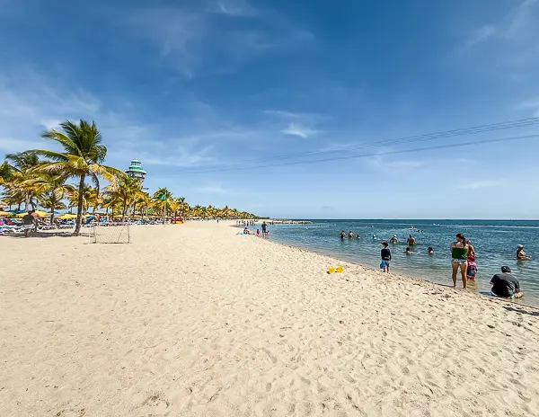 Wide view of the main beach at Harvest Caye, Belize, showing calm blue water and palm trees on Norwegian Cruise Line’s private island.