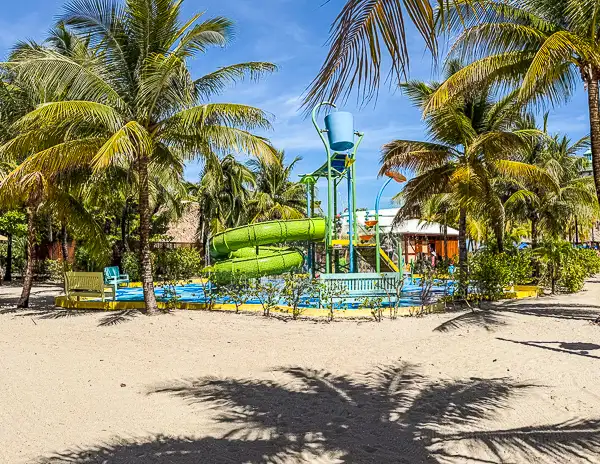 Colorful splash pad and water play area surrounded by palm trees at Harvest Caye, Belize, part of Norwegian Cruise Line’s private island family zone