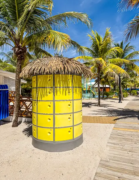 Bright yellow lockers on the sandy path at Harvest Caye, Belize, available for rent near the splash pad and beach area