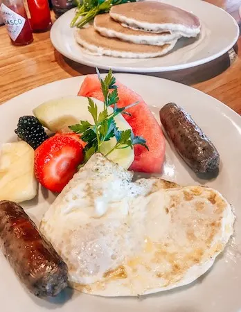 a plate of over medicum eggs with 2 sausages, fresh fruit, and a side plate of pancakes | The Kettle in Manhattan Beach