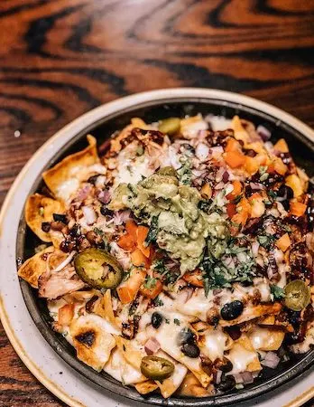 a skillet plate of nachos smothered in pulled pork, beans, jalapenos, cheese, and guacamole | BBQ Pork Nachos from Gus's BBQ in South Pasadena