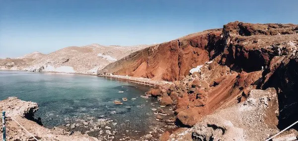 Red lava rock formations surrounding a bay of blue water in Red Beach Santorini Greece