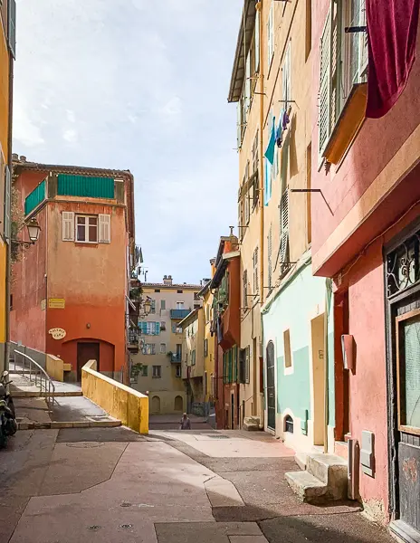 Narrow alleyway in Old Town Nice, France, lined with colorful buildings, shuttered windows, and laundry hanging from balconies.