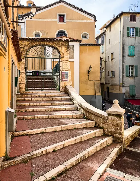 Stone staircase leading to a gated courtyard in Old Town Nice, surrounded by pastel buildings with Mediterranean-style shutters.
