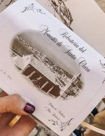 A hand holding a package of cookies from Convento de Santa Clara in Palma de Mallorca, with a vintage-style label displaying an old photograph of the monastery.