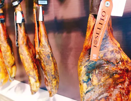 Cured pig legs hanging in shop | Paleta de jamón Joselito