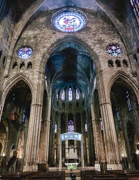 The grand interior of Girona Cathedral in Spain, showcasing its towering Gothic arches, intricate stained glass windows, and the main altar in the distance.