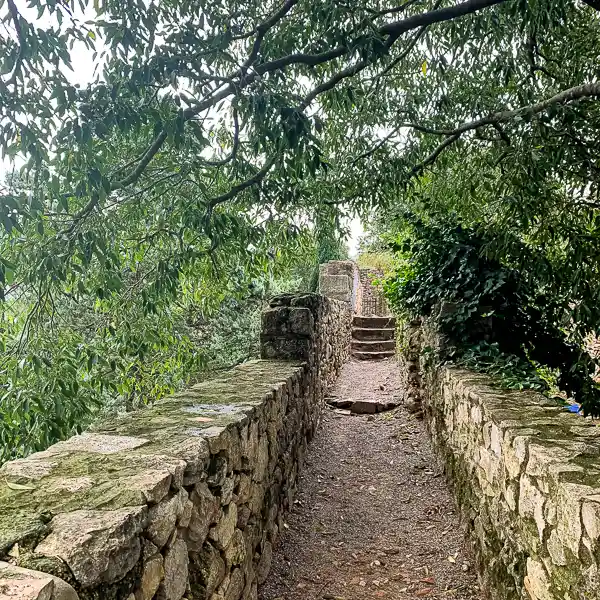 Narrow stone path along the Girona city wall, framed by lush trees.