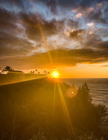 Golden sunset with rays of light shining through the silhouettes of The Cliffs in Kauai