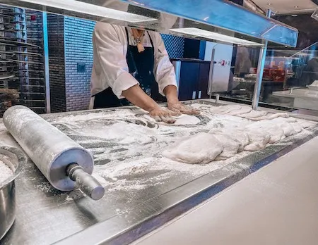 Man kneading pizza dour over floured metal surface