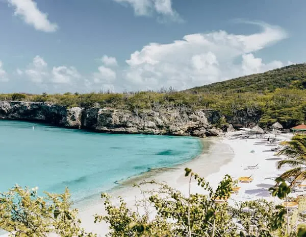 A pristine beach with white sand and blue waters with yellow beach chairs in Curacao