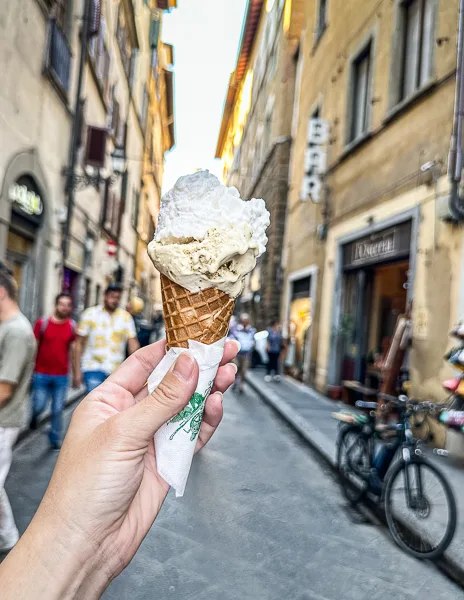hand holding up gelato cone in the middle of a street in florence