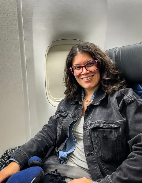 kathy, excited, sitting in plane seat for a flight to take a cruise