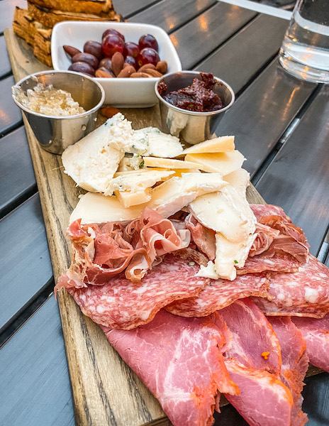 a board topped with sliced meats, cheeses and nuts