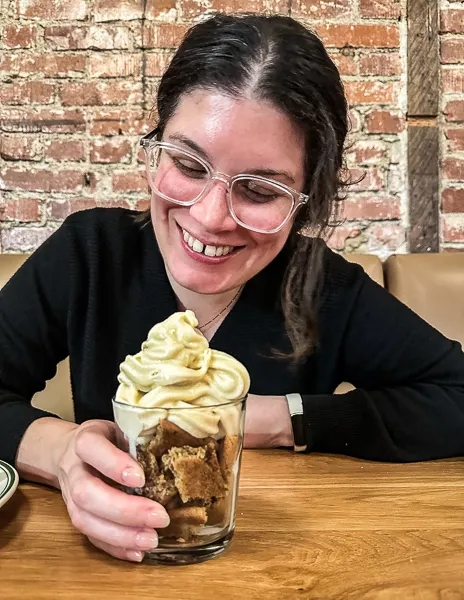 kathy smiling while looking at a glass of what appears to be a cookies-and-cream dessert.