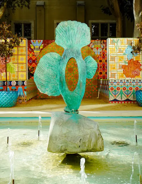 a statue of a green fish in a fountain with colorful tiled artwork in the background