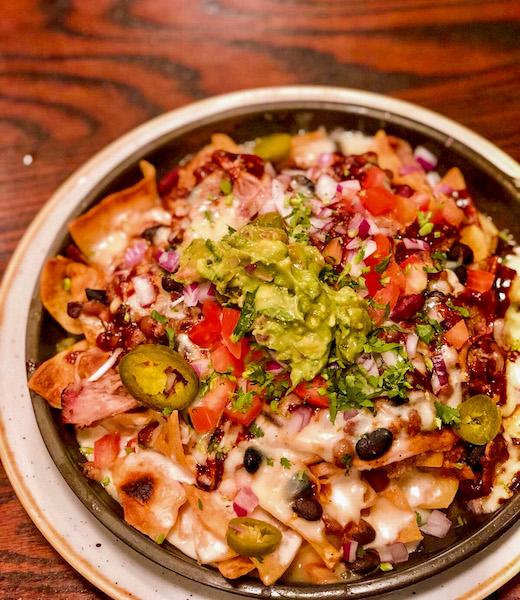 a skillet of nachos with melted cheese and toppings