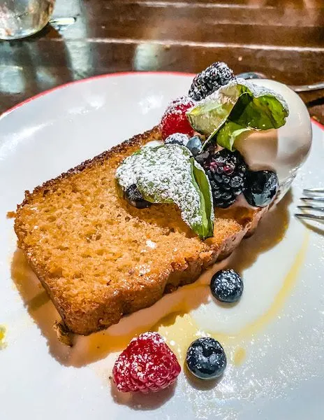 a slice of olive oil cake with berries and a scoop of ice cream on top