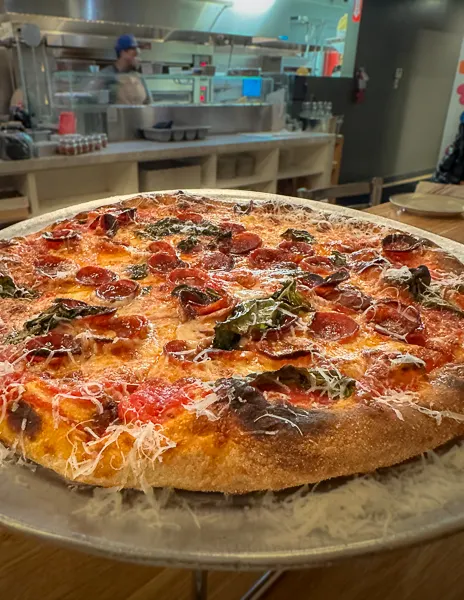 A pizza with pepperoni and basil on a stand, ready to be served.