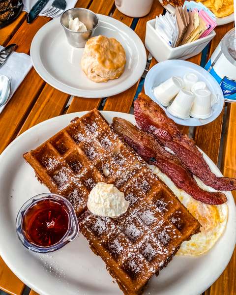 breakfast plate of waffles, bacon, eggs and syrup