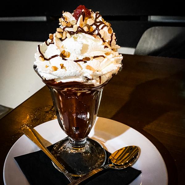 hot fudge sundae topped with whip cream, nuts and a cherry