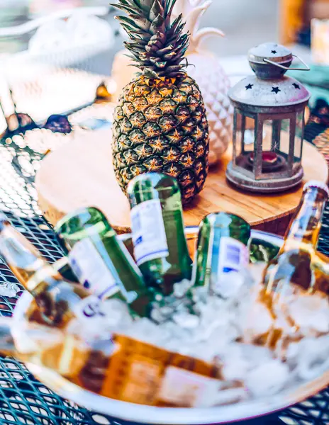 a bucket of beers in ice set over a table with a pineapple and cute metal lantern