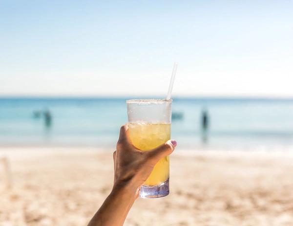 woman holding up a margarita at the beach