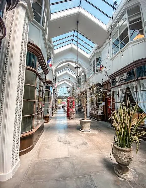 Interior view of the Burlington Arcade in Pasadena, featuring a charming walkway with skylights, potted plants, and boutique shops lining the sides.