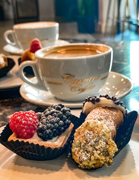 mini fruit tart, cannoli and a cup of coffee with carrara's coffee labeled in gold
