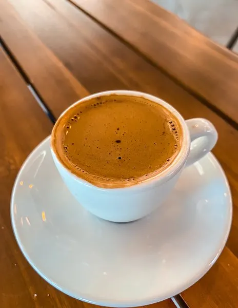 A rich and creamy choco espresso served in a white ceramic cup on a saucer, placed on a wooden table at a café in Pasadena.