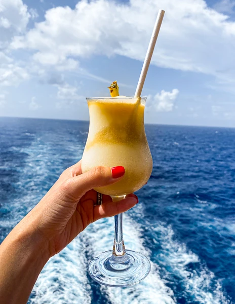 hand holding a pina colada with the ocean in the background