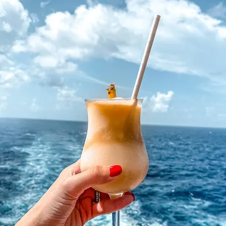 hand holding a pina colada with the ocean in the background