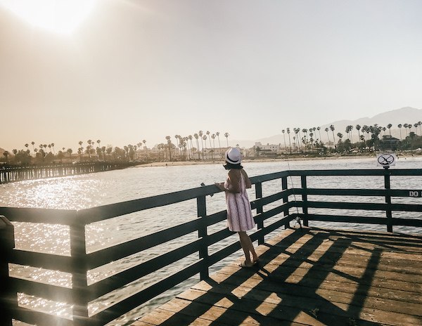 kathy looking over the railing of a pier towards the coast and palm trees