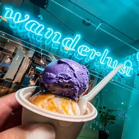 small cup of 2 scoops of ice cream, top scoop is purple and the sign behinds it glows wanderlust