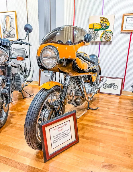 A vintage 1974 Ducati 750 Sport motorcycle on display in a museum, with information plaque in front.