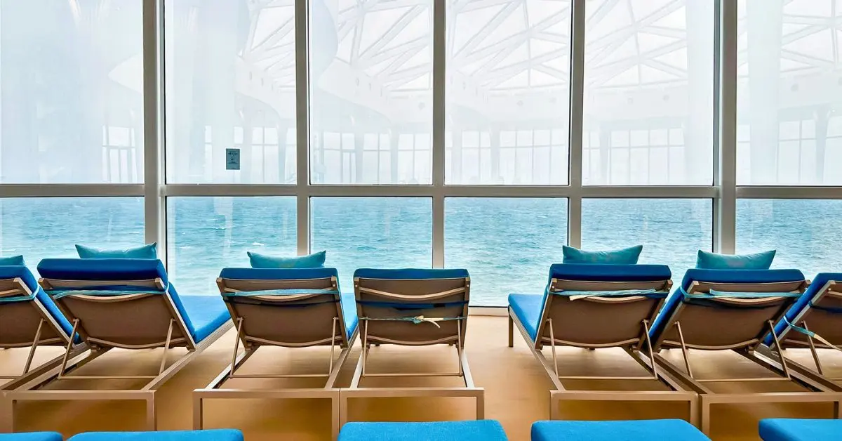 Indoor lounge chairs facing the ocean through large panoramic windows, offering a serene view during cruising in fall or winter.