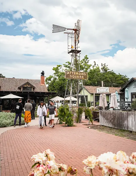 Pedestrians stroll through Atterdag Square in Solvang, marked by a rustic windmill and a welcoming sign