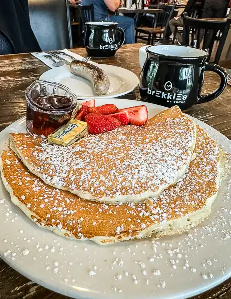 thin pancakes lovely covered in powered sugar, plated with a black mug on the side with Brekkies on it