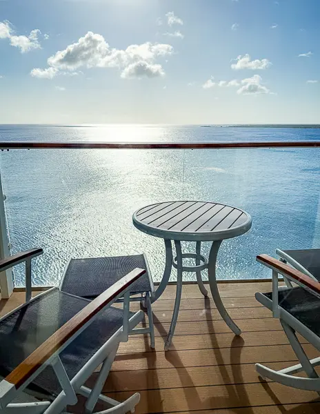 Sunny cruise ship balcony with two chairs and a small round table overlooking the calm ocean, captured during an off-season sailing.