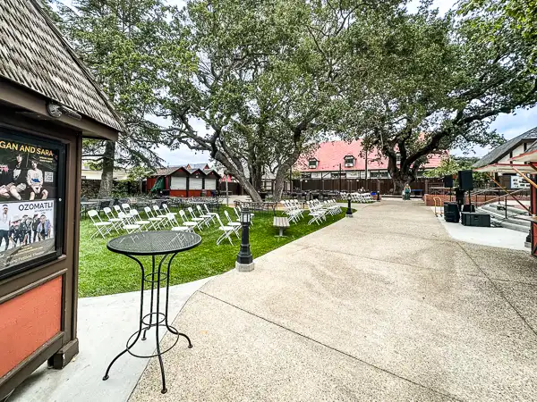 outdoor seating area set up for an event with rows of chairs facing a stage, nestled among mature trees at the Solvang Festival Theater