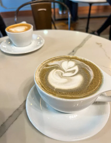 Two lattes served at Republik Coffee Lounge in Pasadena, featuring intricate latte art on white marble tabletops in a cozy café setting.