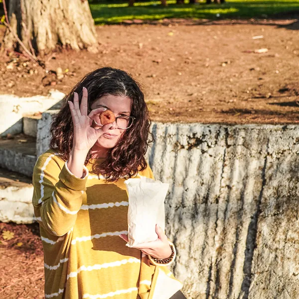 woman holding up a mini apple cider donut over her eye