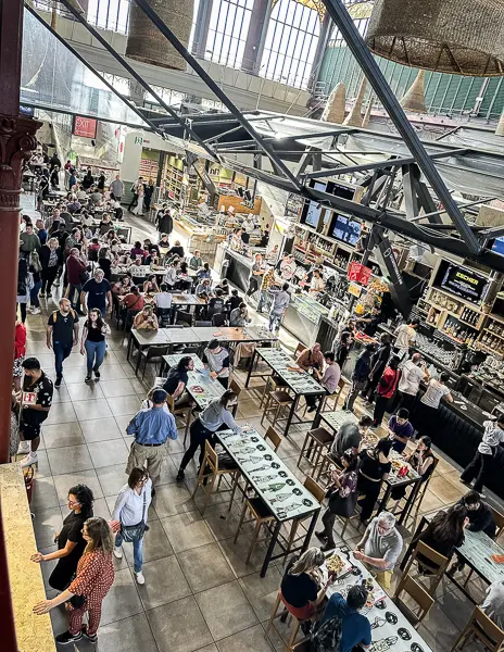 The bustling interior of Mercato Centrale in Florence, a vibrant food hall where locals and tourists alike gather around communal tables, with diverse food stalls lining the space under an industrial-chic ceiling.
